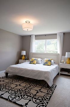 a white bed sitting in a bedroom next to a window with yellow and blue pillows