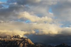 the mountains are covered in snow and clouds as the sun is shining down on them