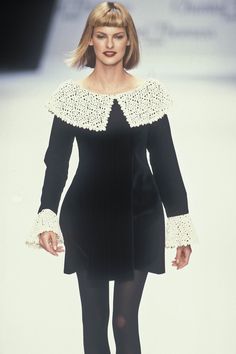 a woman walking down a runway wearing black and white clothing with lace detailing on her shoulders