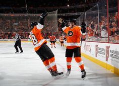 two hockey players in orange and black uniforms on the ice with their arms raised up