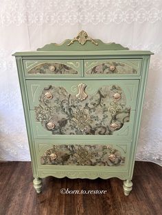 an old dresser painted in green and gold with floral designs on the front, along with white wallpaper