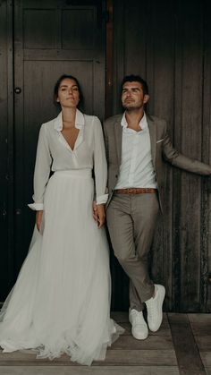 a man and woman standing next to each other in front of a wooden wall holding hands