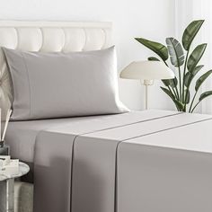 a white bed with grey sheets and pillows