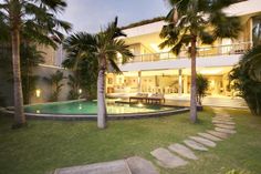 the house is surrounded by palm trees and has a swimming pool in front of it