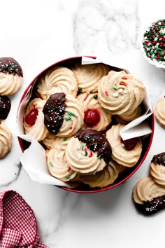 a red bowl filled with cookies on top of a white marble counter topped with sprinkles