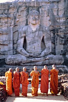 five monks standing in front of a large statue with their backs turned to the side