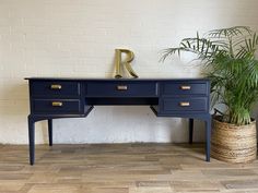 a blue desk with gold handles next to a potted plant and a brick wall