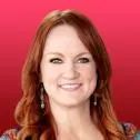 a woman with long red hair smiling at the camera while wearing a floral shirt and earrings