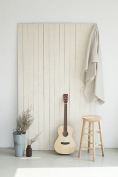 an acoustic guitar sits next to a stool in front of a wall with white boards