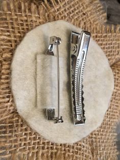 two silver hair clips sitting on top of a piece of burlied fabric next to each other