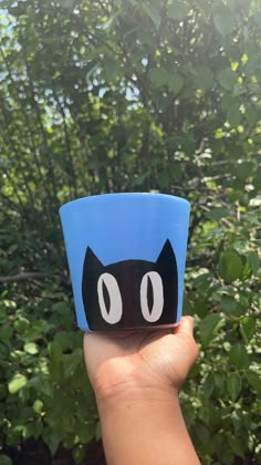 a hand holding up a blue cup with a black cat face on it