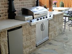 an outdoor bbq with grill and table next to brick wall, chairs and tables