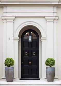 two large planters are in front of a black door with arched doorway and window