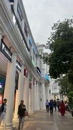 people walking down the sidewalk in front of a building with columns and signs on it