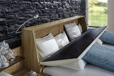 a bed that has pillows on it in front of a brick wall with a window