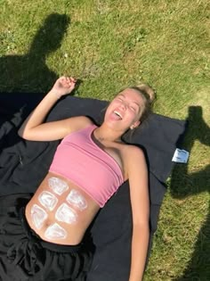 a woman laying on top of a black blanket in the grass with white patches on her stomach