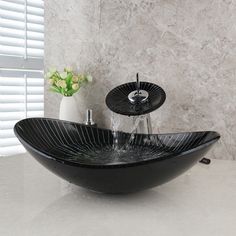 a black bowl sink sitting on top of a counter next to a vase with flowers