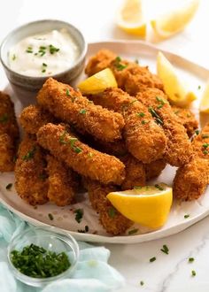 fried chicken sticks with lemon wedges and ranch dressing on a white plate next to small bowl of ranch dressing