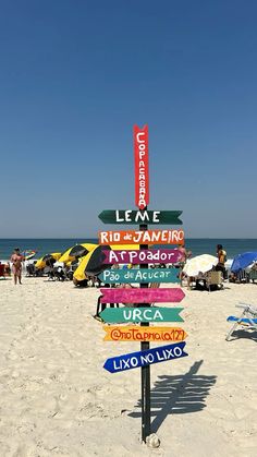 a sign post on the beach that has many different colored signs in front of it