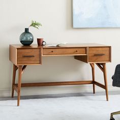 a wooden desk sitting in front of a painting on the wall next to a chair