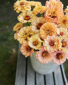 a vase filled with yellow and pink flowers on top of a wooden bench in the grass