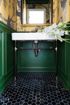 a bathroom with green walls, black and white flooring and a gold framed mirror