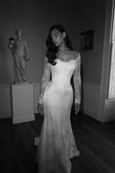 a woman in a long sleeved wedding dress standing on a wooden floor next to a statue