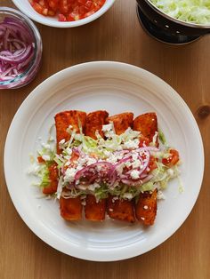 a white plate topped with tofu covered in lettuce next to bowls of salad