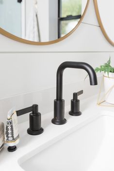 a bathroom sink with two black faucets and a round mirror above the sink