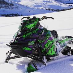 a green and black snowmobile parked on the side of a snowy hill with mountains in the background