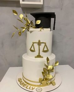 a three tiered cake decorated with gold leaves and a judge's hat on top