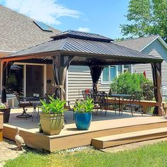 a gazebo sitting on top of a wooden deck in front of a house with potted plants