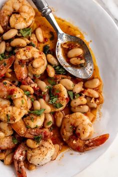 a white plate topped with shrimp, beans and garnished with parsley next to a spoon