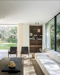 a living room with white couches and wooden tables in front of large windows that look out onto the backyard