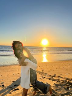 a man and woman hug on the beach at sunset