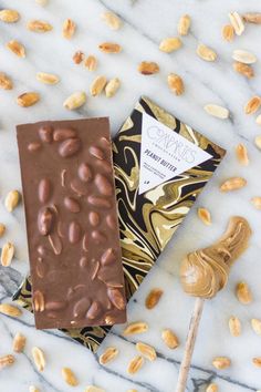 the chocolate bar has nuts on it and is next to a spoon with peanut butter