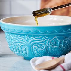 a spoon is pouring oil into a blue bowl on the counter next to a bottle of water