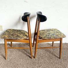 two wooden chairs sitting next to each other on top of a carpeted floor in front of a white wall