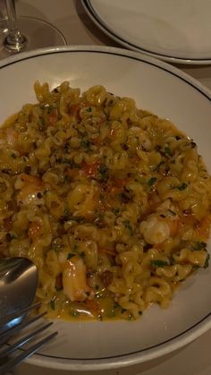 a white plate topped with pasta and shrimp next to silverware on top of a table