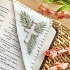 a cross is embroidered on top of an open book next to flowers and a wicker basket