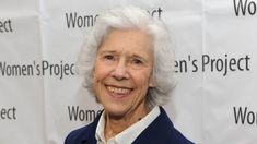 an older woman standing in front of a wall with women's project on it