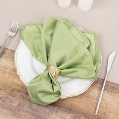 a place setting with green napkins and silverware on a wooden tablecloth covered plate