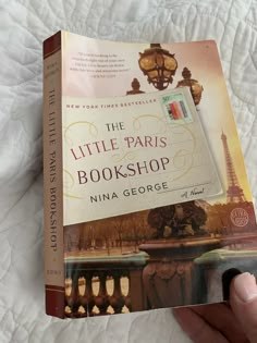 the little paris bookshop by nina george is in someone's hand on a bed