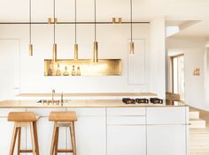 two wooden stools sit in front of a kitchen island with gold lights hanging from the ceiling