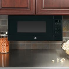 a black microwave oven sitting on top of a counter next to a bowl of popcorn