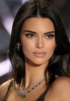 a woman with dark hair wearing a necklace and red lipstick on the catwalk at a fashion show