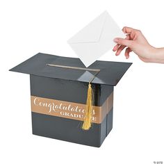 a hand is holding a piece of paper above a box that has an envelope in it