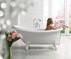 a woman sitting in a bathtub next to a window with pink flowers on it