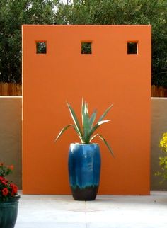 a blue vase with a plant in it next to an orange wall and some flowers