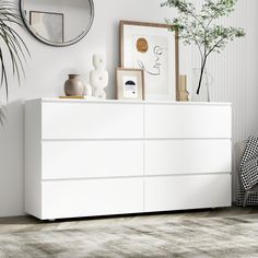 a white dresser sitting in a living room next to a mirror and potted plant